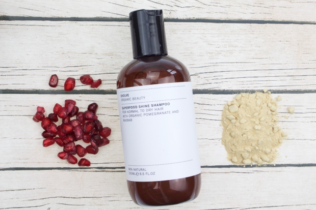 Evolve shampoo bottle on wooden floorboards with pomegranate seeds and baobab powder