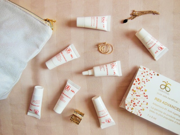 Arbonne RE9 Advanced skincare mini tubes flatlay on a stripy beige background