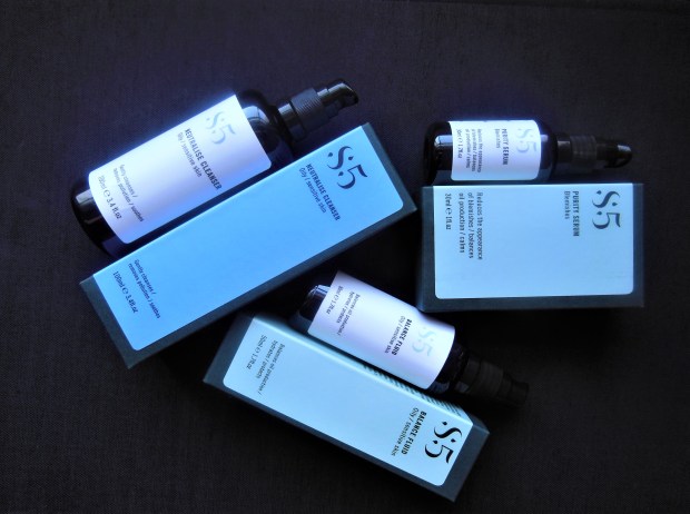 Three skincare products and boxes on a black background