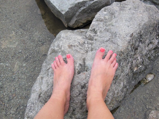 Feet with coral pedicure on a rock